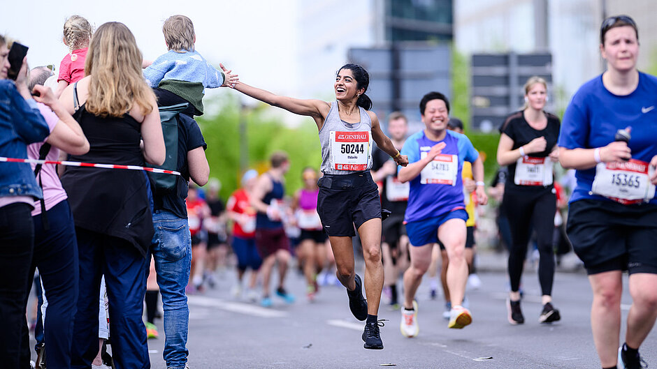 GENERALI BERLINER HALBMARATHON 2024: Läuferin auf der Strecke klatsch mit Zuschauenden ab © SCC EVENTS / Marvin Ibo Güngör