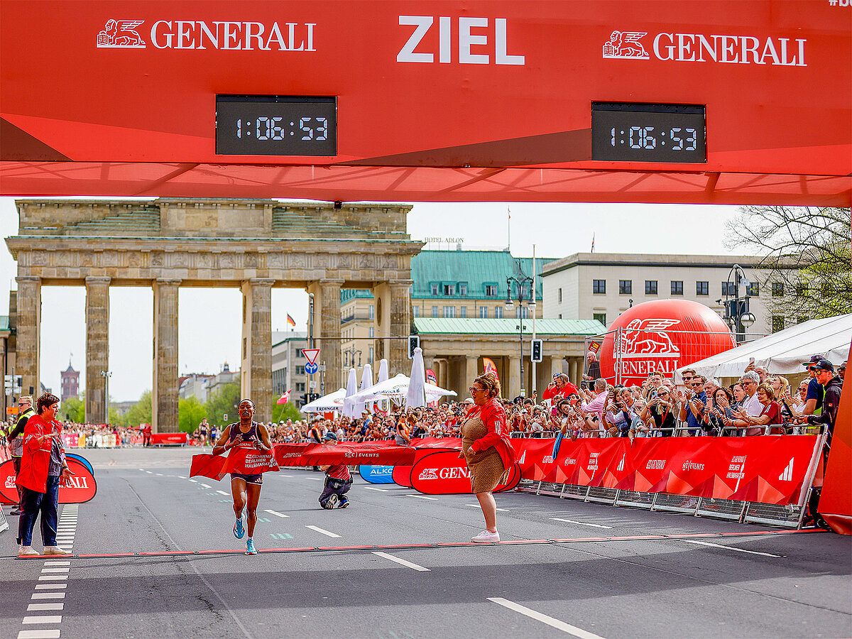 Street view of finish line with spectators and a single runner.