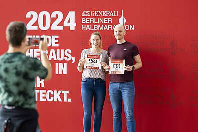 GENERALI BERLINER HALBMARATHON Inlineskating 2024: Teilnehmerpärchen hält vor der GENERALI Fotowand die Startnummern in die Kamera © SCC EVENTS / Jean-Marc Wiesner