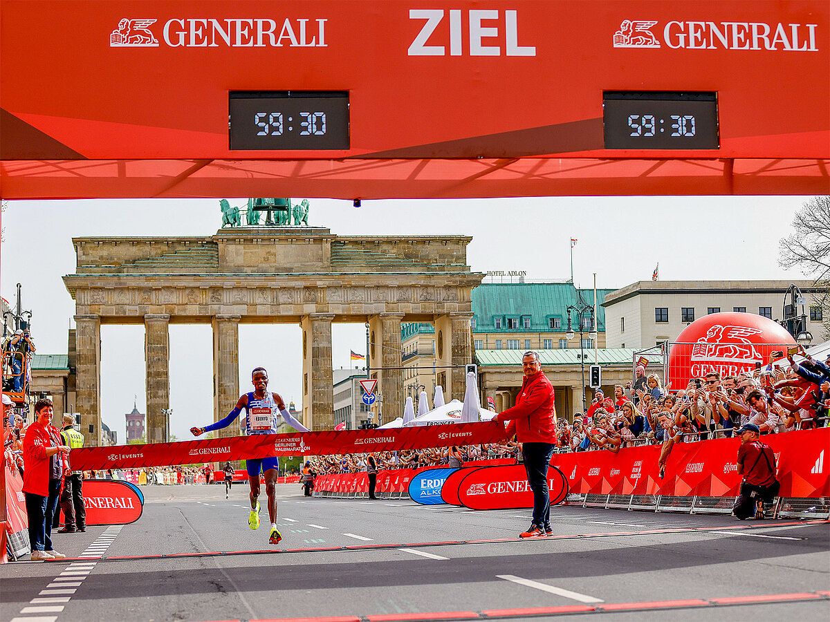 Street view of finish line with spectators and a single runner.